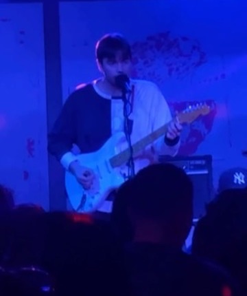 A Darksoft guitarist singing and playing a white Stratocaster on stage under blue light