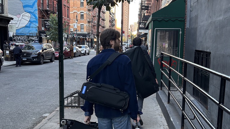 A Darksoft band member walking down a Lower East Side sidewalk carrying guitar cases before the show